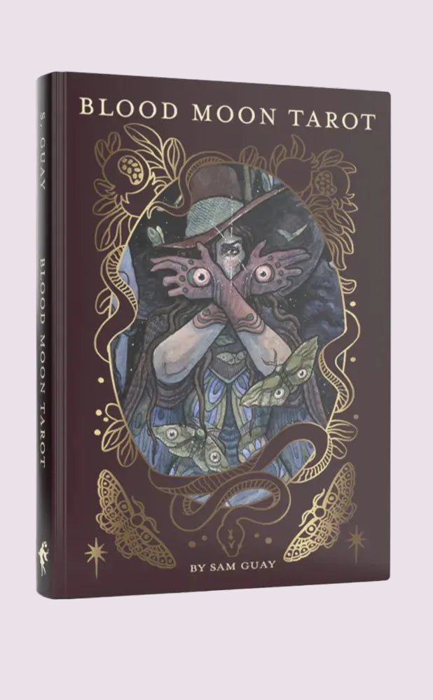 Book titled 'Blood Moon Tarot' with a cover illustration of a person holding their hands over their eyes, surrounded by decorative elements.