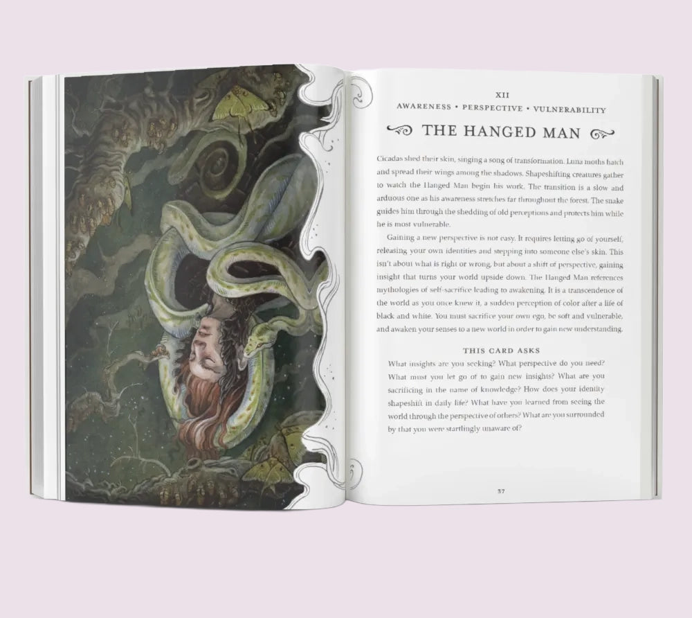 Open Blood Moon Tarot book showing an illustration of 'The Hanged Man' tarot card on a light pink background