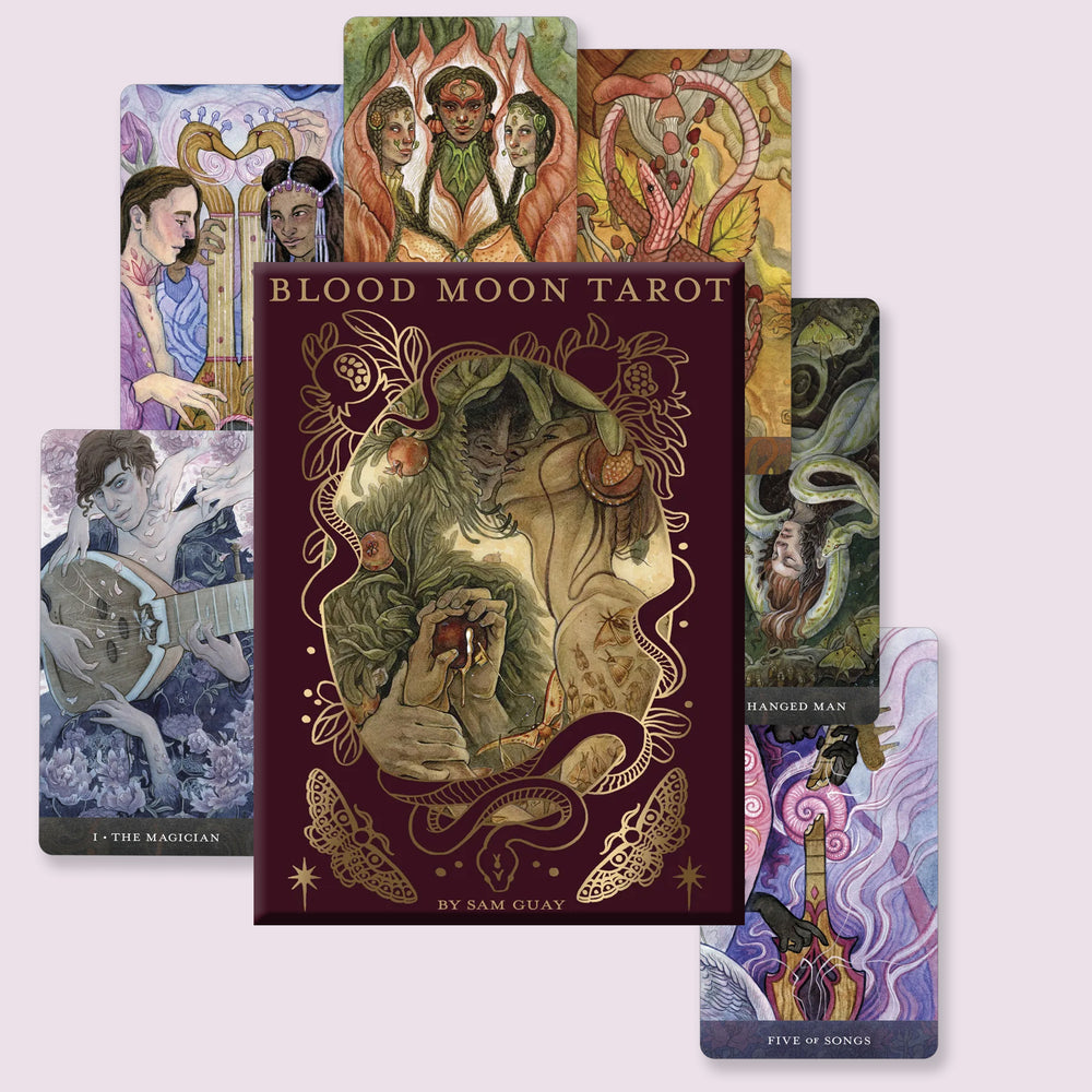 Blood Moon Tarot deck box in deep burgundy with gold detailing, shown with a spread of illustrated cards displaying the deck’s expressive artwork and borderless design.