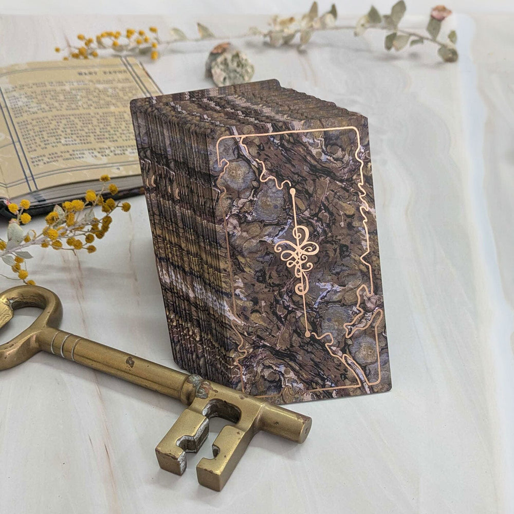 Oracle of Many Paths by James R. Eads stacked deck showing marbled card backs with rose gold detailing beside antique brass key.